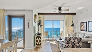 Un salon spacieux avec un balcon donnant sur la mer, un ventilateur de plafond et un coin repas.