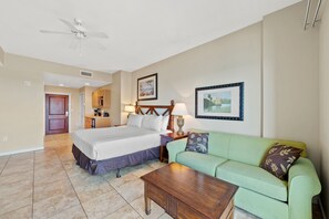 A hotel room with a bed, a green sofa, a wooden coffee table, a ceiling fan, and framed pictures on the walls.