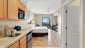 Habitación de hotel con kitchenette, una cama, un balcón con vistas y una puerta que da a otra habitación.