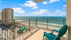 Ein Balkon mit Blick auf Strand und Meer, ein grüner Stuhl und ein Gebäude im Hintergrund.