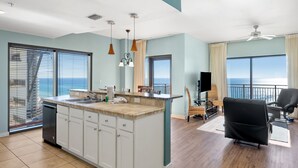A modern kitchen with a large island, a dining area with a view, and a living room with a black sofa. - Origin 1404 - One Bedroom - Amazing Gulf View (Panama City Beach)