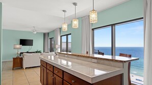 A modern kitchen with a large island, pendant lights, and a view of the ocean.