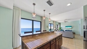 A kitchen with a large island, a dining area with a view, and a living area with a TV. - Origin 1604 -PENTHOUSE- 3 Bedroom- Private Large Sunset Deck (Panama City Beach)