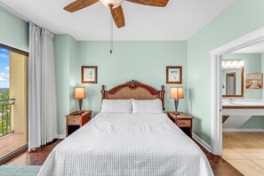 Een slaapkamer met een groot bed, een houten hoofdbord, twee nachtkastjes met lampen, een plafondventilator en uitzicht op de omgeving.