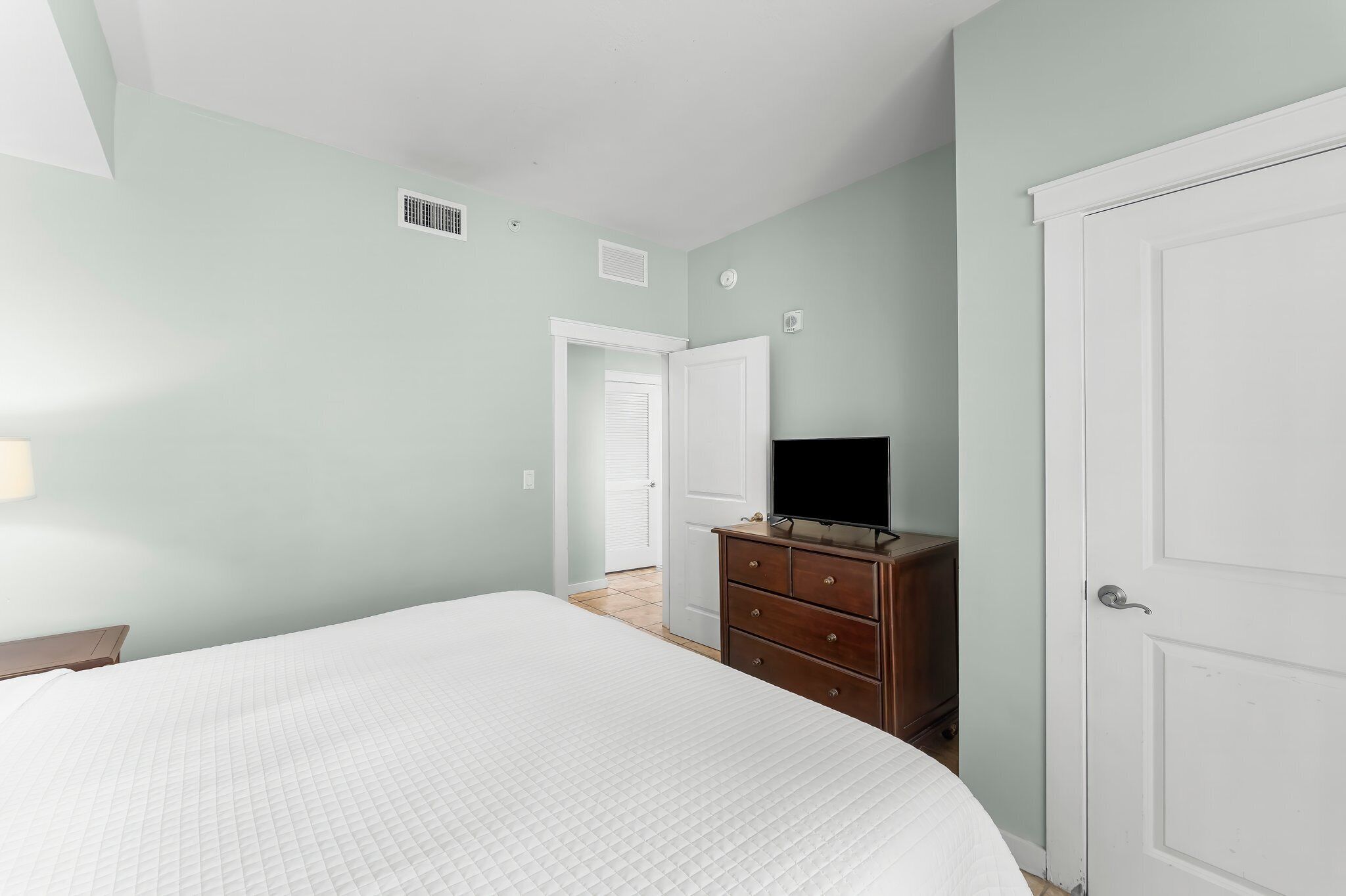 Un dormitorio con cama, cómoda, televisor y una puerta.