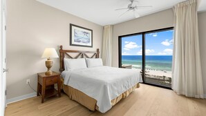 A bedroom with a bed, a nightstand, a lamp, a ceiling fan, and a large window with a beach view. - Origin 0601/603 - Two Bedroom Lock Out with Sunset and Gulf Views (Panama City Beach)
