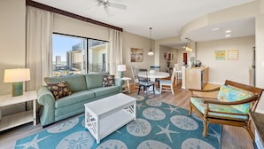 A spacious living area with a sofa, coffee table, and a dining table with chairs. A ceiling fan and pendant lights are visible.
