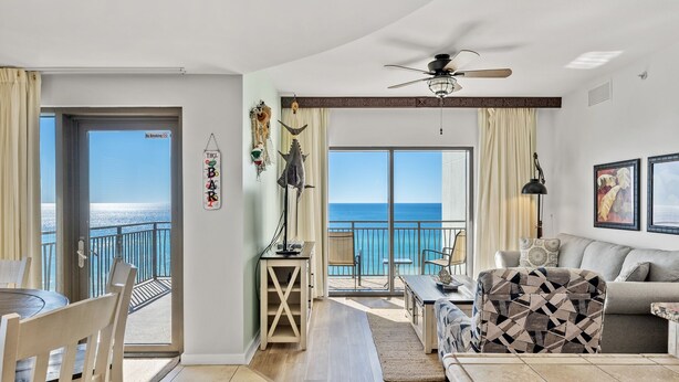A spacious living room with a balcony overlooking the sea, a ceiling fan, and a dining area.