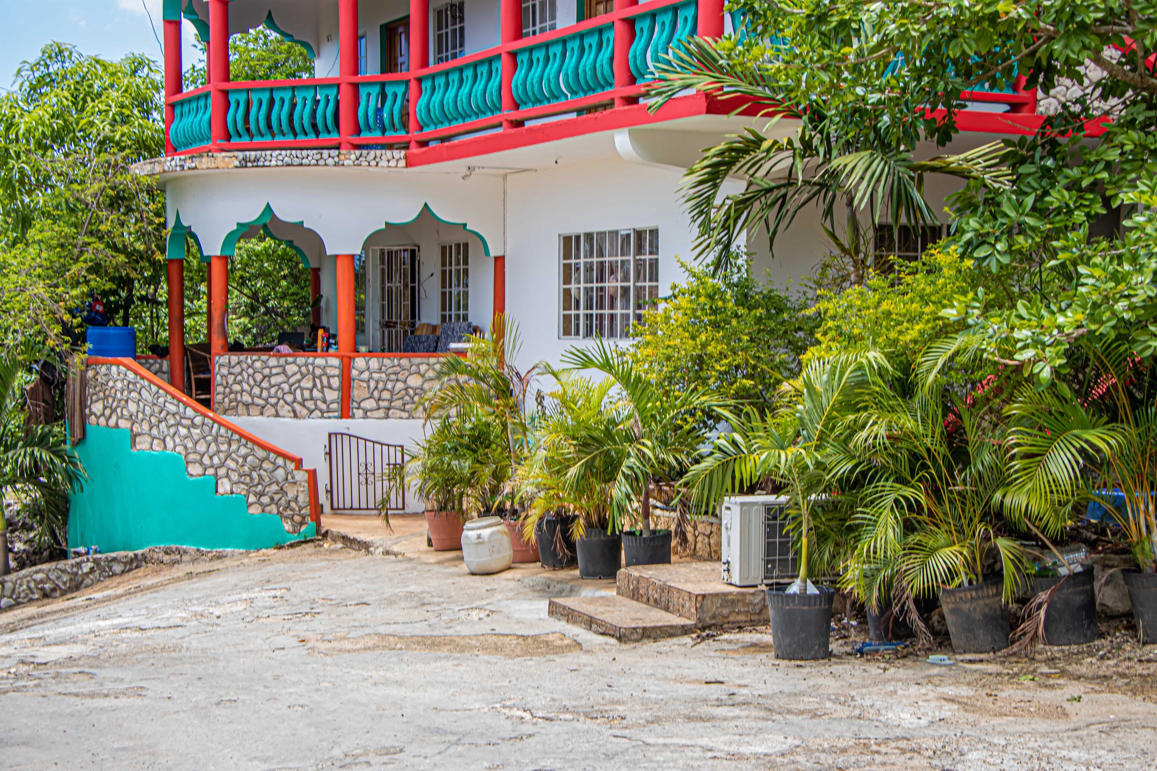 A two-story building with a balcony, stone steps, and potted plants.