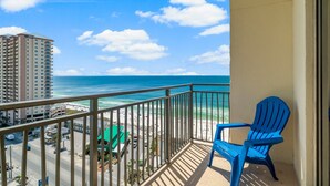 A balcony with a view of the beach and ocean, a blue chair, and a building in the background. - Origin 1333/1335 - Three Bedroom Gulf View Connector Unit- Stunning Gulf Views (Panama City Beach)