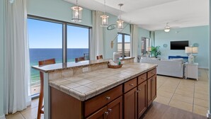 A spacious kitchen with a large island, a dining area with a view of the ocean, and a living room with a flat-screen TV. - Origin 1602/1604- PENTHOUSE 6 Bedroom - One of a kind unit - TWO Large Decks (Panama City Beach)