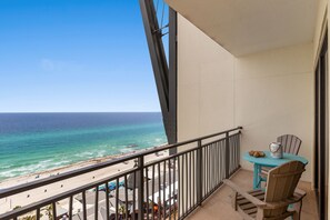 Un balcon avec vue sur l’océan et la plage, une petite table avec des chaises et un vase décoratif.