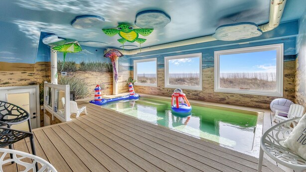 Un espace piscine doté d’une terrasse en bois, d’un poste de surveillance pour les sauveteurs et offrant une vue sur la plage grâce à de grandes fenêtres.