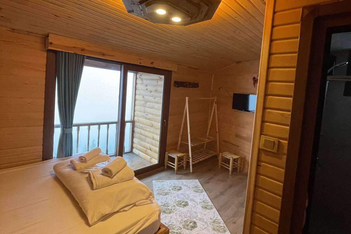 A wooden cabin room with a bed, a small table, and a window.