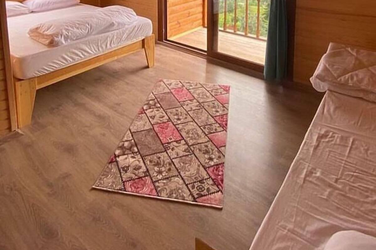 A wooden cabin room with a bed, a small table, and a view of the outdoors.
