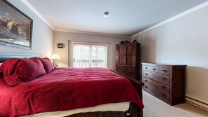 Un dormitorio con una cama grande, un aparador de madera, un cuadro en la pared y una ventana con persianas.