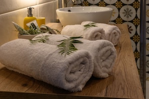 A bathroom with a wooden vanity, a white sink, and neatly folded towels with rosemary sprigs. - La Catalane (Theza)