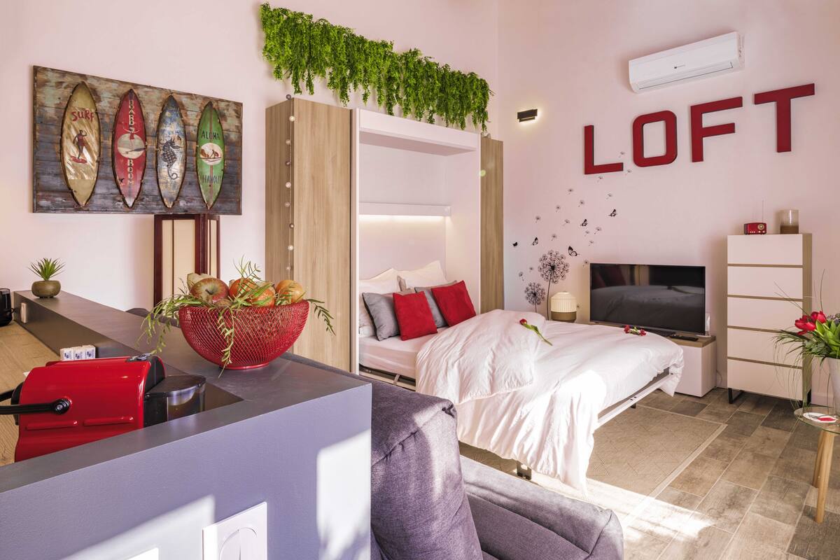 A modern hotel room with a bed, a desk, a TV, and a wall-mounted plant.