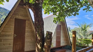 A wooden cabin with a large tree in front, a metal roof, and a wooden fence. - Raio de Sol Pousada & Camping (Angra dos Reis)