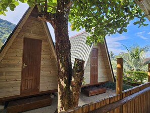 A wooden cabin with a large tree in front, a metal roof, and a wooden fence. - Raio de Sol Pousada & Camping (Angra dos Reis)