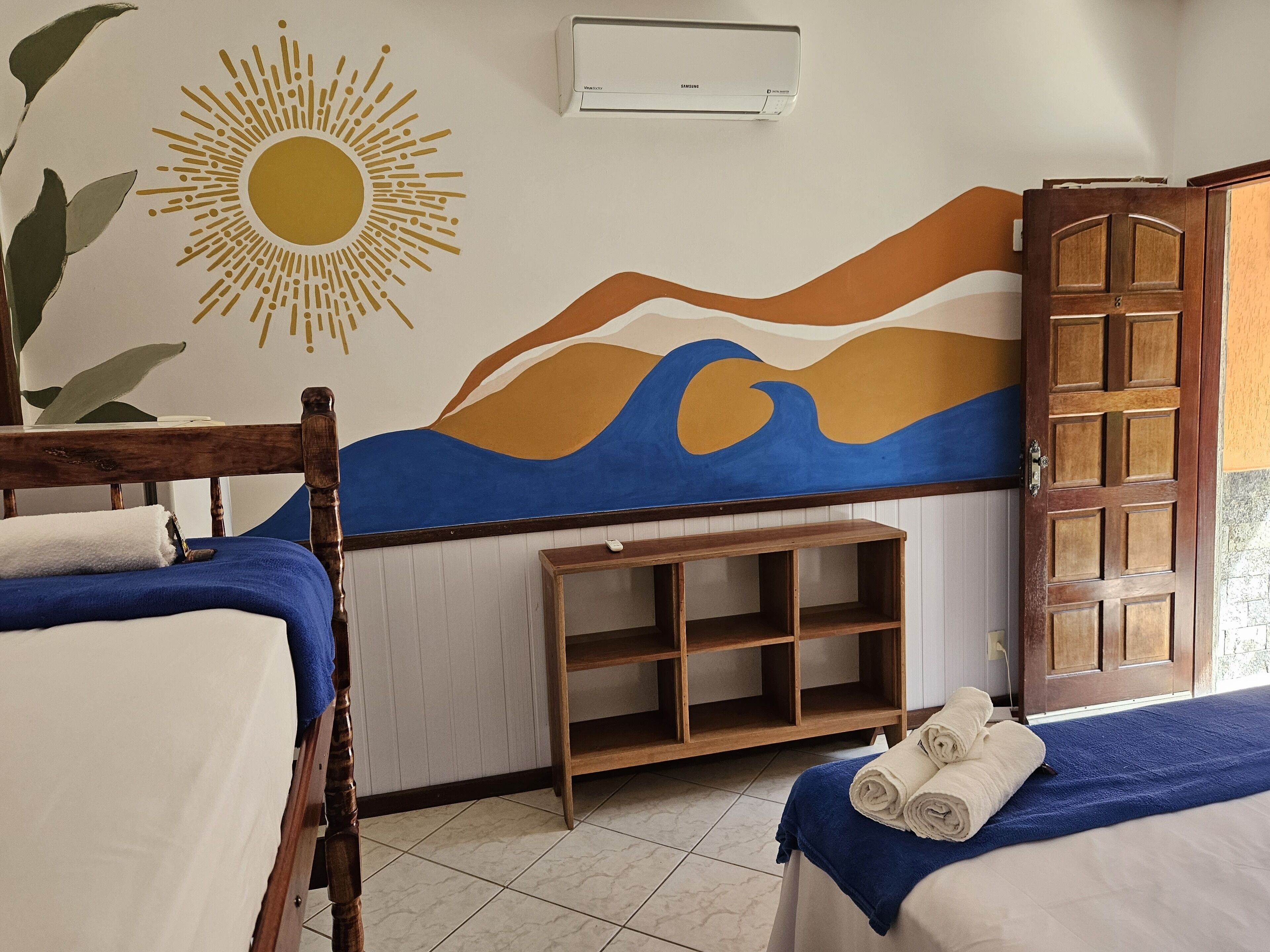 A hotel room with two beds, a wooden headboard, a wall mural, a wooden shelf, and a door.