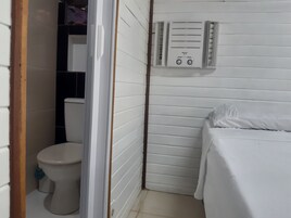 Um banheiro pequeno e branco, com vaso sanitário, chuveiro e uma cama.