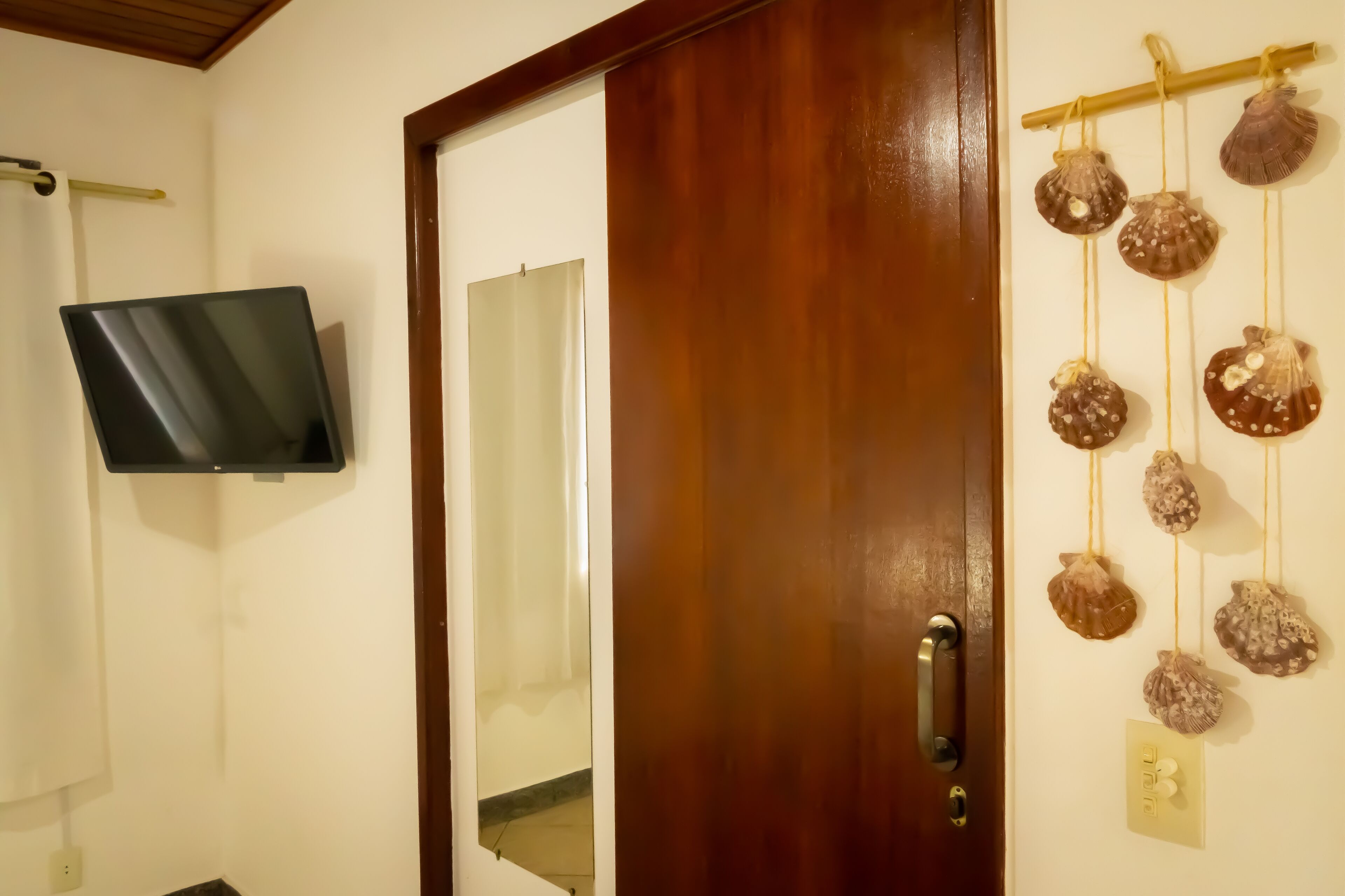 Quarto com porta de madeira, televisão montada na parede e interruptor de luz fixado.
