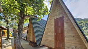 A row of wooden triangular cabins with metal roofs, set against a backdrop of trees and hills. - Raio de Sol Pousada & Camping (Angra dos Reis)