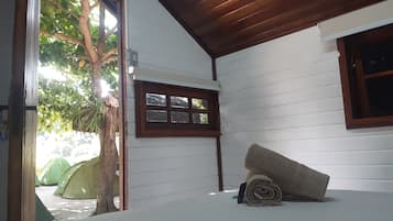 A room with a wooden ceiling, a window with a wooden frame, a tree outside, and a tent in the background.