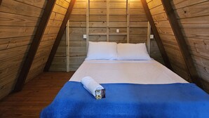 A cozy attic bedroom with a wooden sloped ceiling, a bed with white bedding, and a blue throw blanket. - Raio de Sol Pousada & Camping (Angra dos Reis)