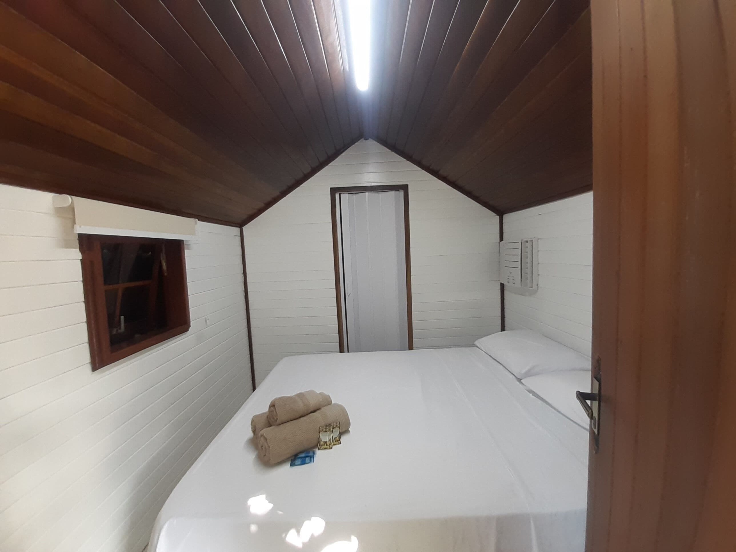 Een klein, eenkamerchalet met een schuin dak, een raam, een deur en een bed met opgerolde handdoeken.