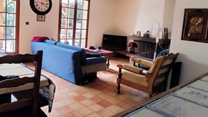 Ein geräumiges Wohnzimmer mit einem blauen Sofa, Holzstühlen, einem Esstisch und einem Kamin.