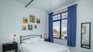 Ein Schlafzimmer mit Bett, Nachttisch, einem Fenster mit Vorhängen und Wandbildern.