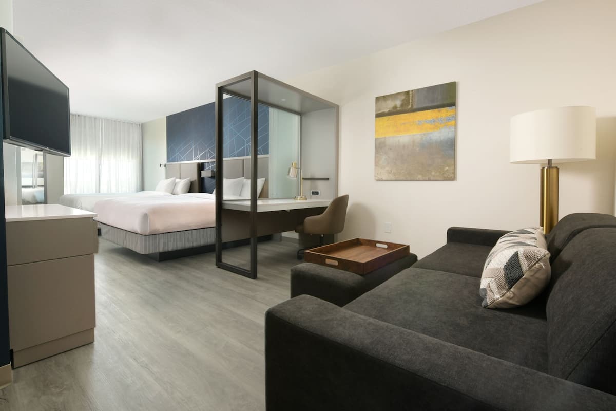 Quarto de hotel moderno com cama, escrivaninha, sofá e televisão.