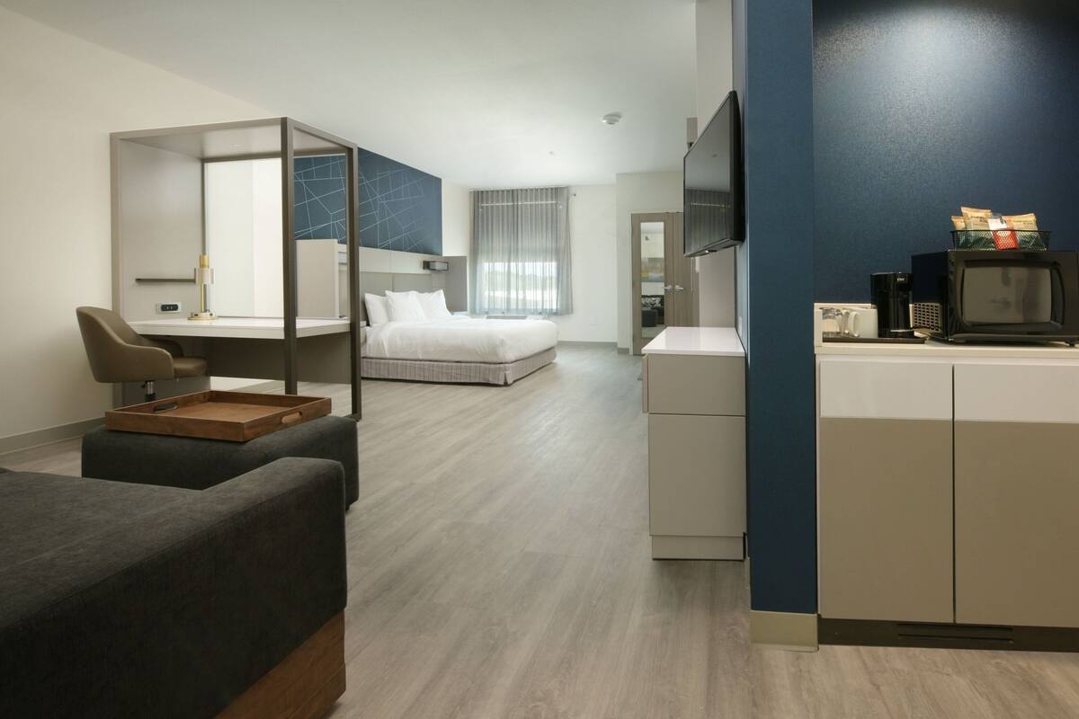Quarto de hotel moderno com uma cama, uma escrivaninha com cadeira, uma TV e um micro-ondas.
