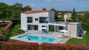 Una casa moderna de dos pisos con piscina, mobiliario exterior y un muro de piedra.