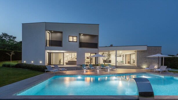 Una casa moderna de dos pisos con piscina, mobiliario exterior e interior bien iluminado.