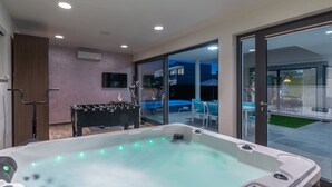 Un área de piscina interior moderna con un jacuzzi, mesa de fútbol y televisor montado en la pared.