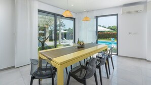 Un comedor moderno con una mesa amarilla y sillas negras, ventanas amplias y vista a una piscina.