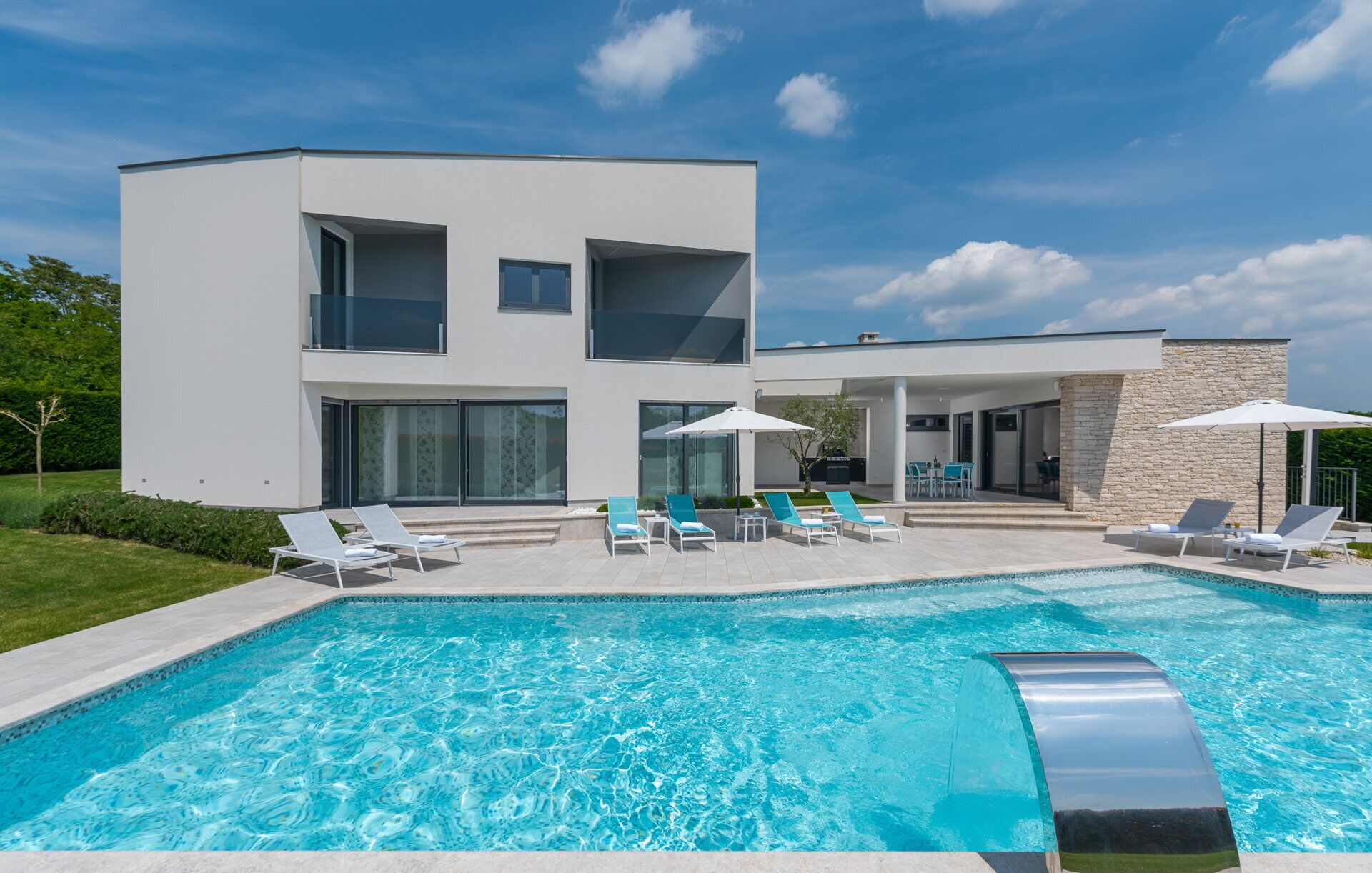Une maison moderne à deux étages, dotée d’une piscine, d’un espace extérieur aménagé et d’un mur en pierre.