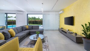 Una sala de estar moderna con un sofá seccional, una mesa de centro y un televisor de pantalla plana montado en una pared amarilla.