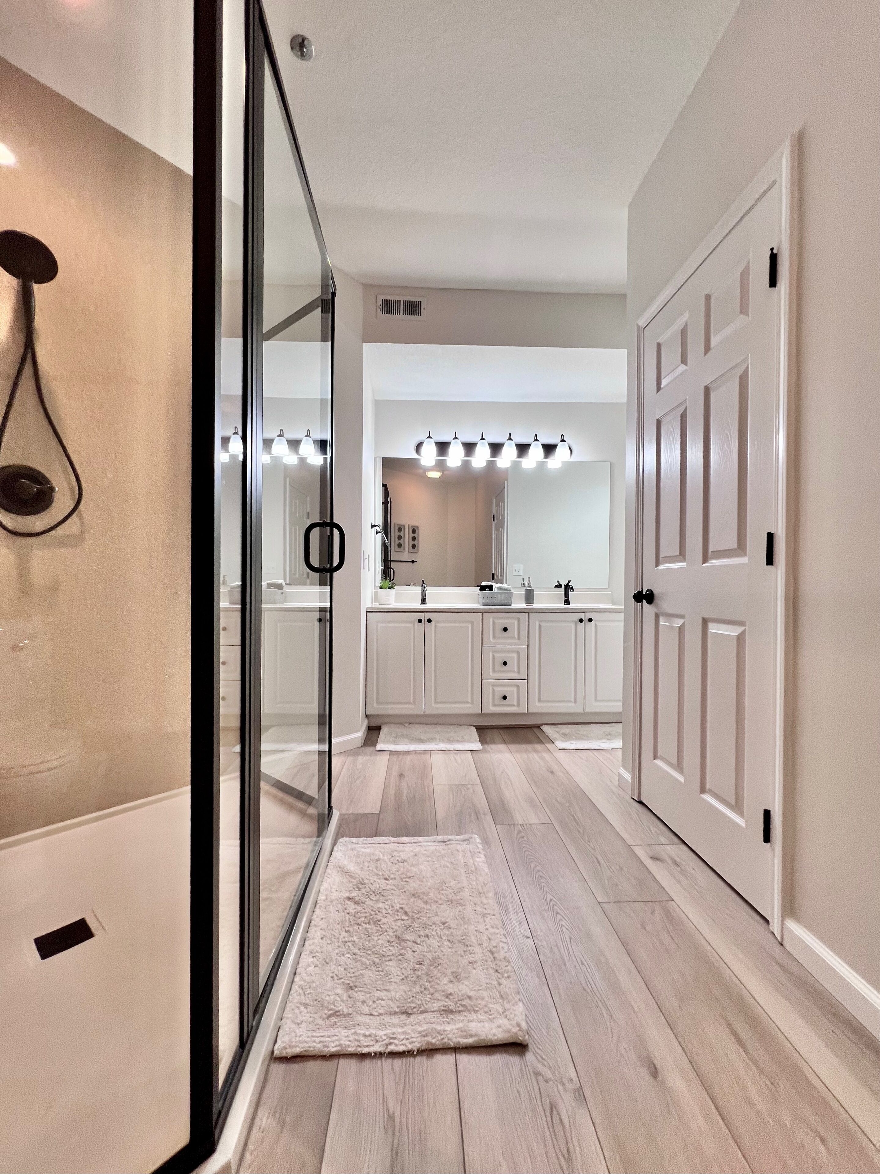 A modern bathroom with a glass shower, white cabinets, and a vanity with a mirror and lights.
