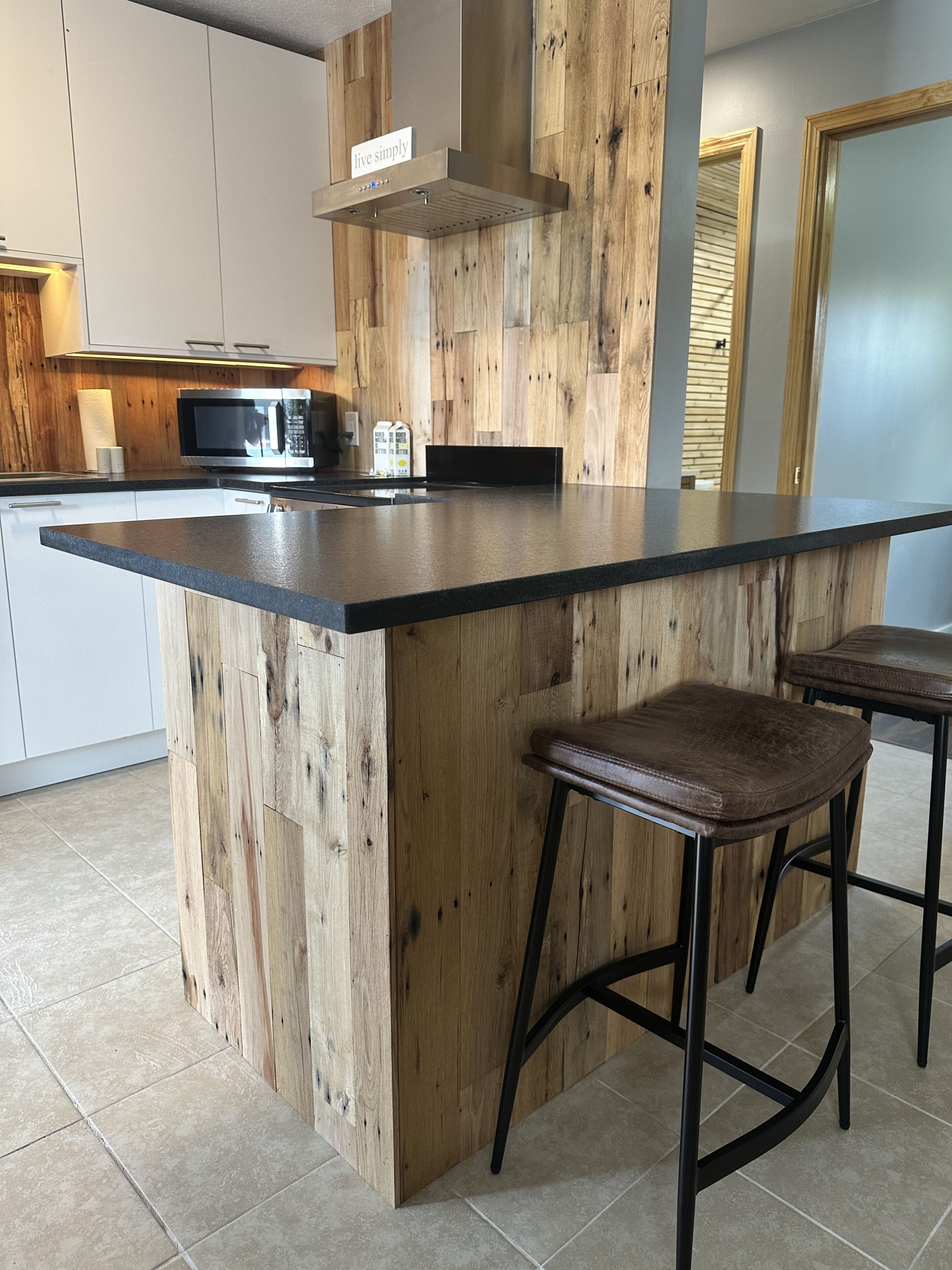 A modern kitchen with a wooden island, bar stools, a microwave, and a stainless steel range hood.