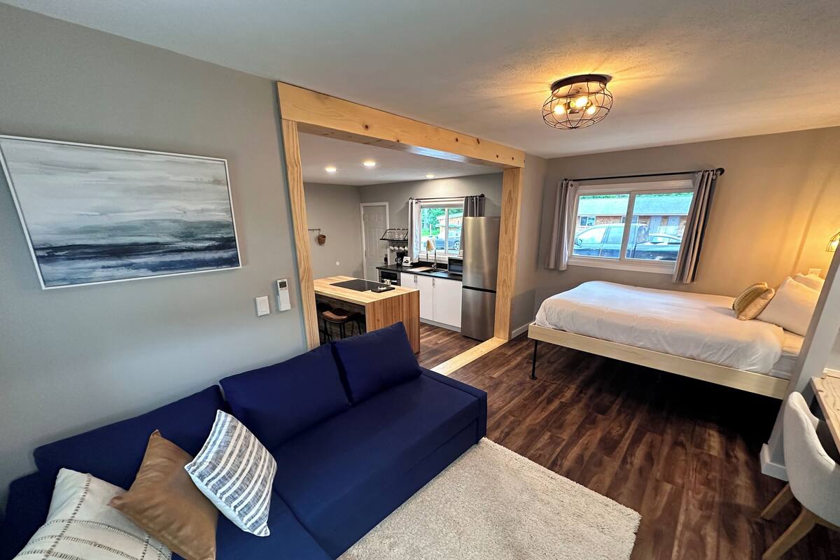 Une pièce de taille modeste comprenant un lit, un canapé, une petite kitchenette et donnant sur l’extérieur.