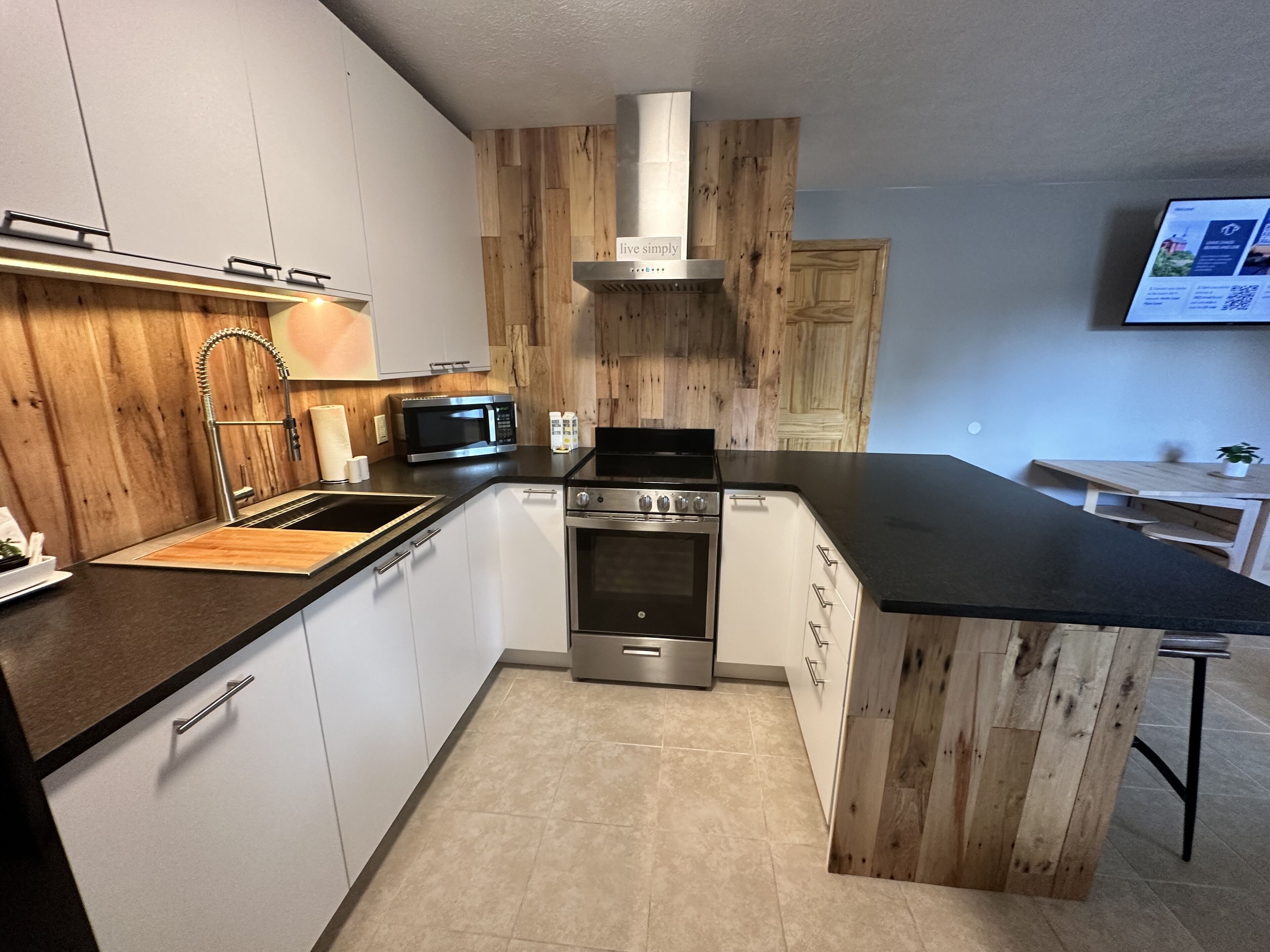 Una cocina moderna con gabinetes blancos, estufa de acero inoxidable, microondas y detalles de madera.