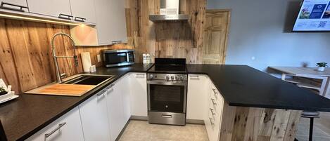 Una cocina moderna con gabinetes blancos, estufa de acero inoxidable, microondas y detalles de madera.