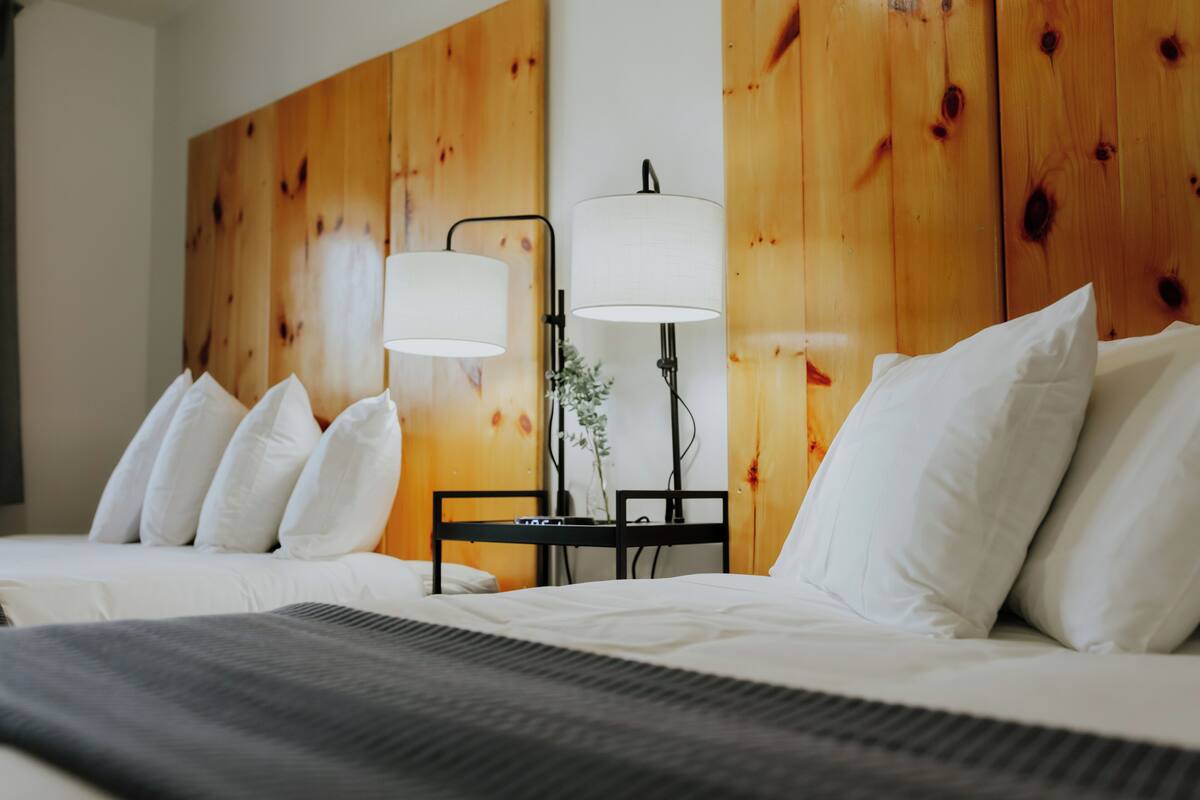 Une chambre d’hôtel avec une tête de lit en bois, un lit avec une literie blanche et deux lampes de chevet.
