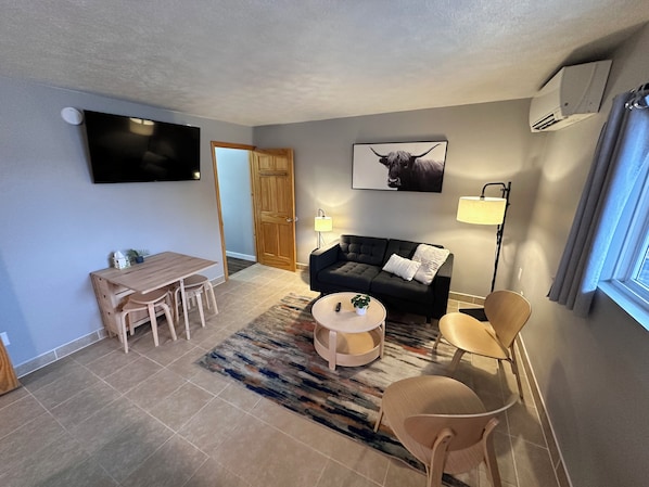 A modern living room with a sofa, coffee table, and a dining area with chairs. - North Coast Place (Marquette)