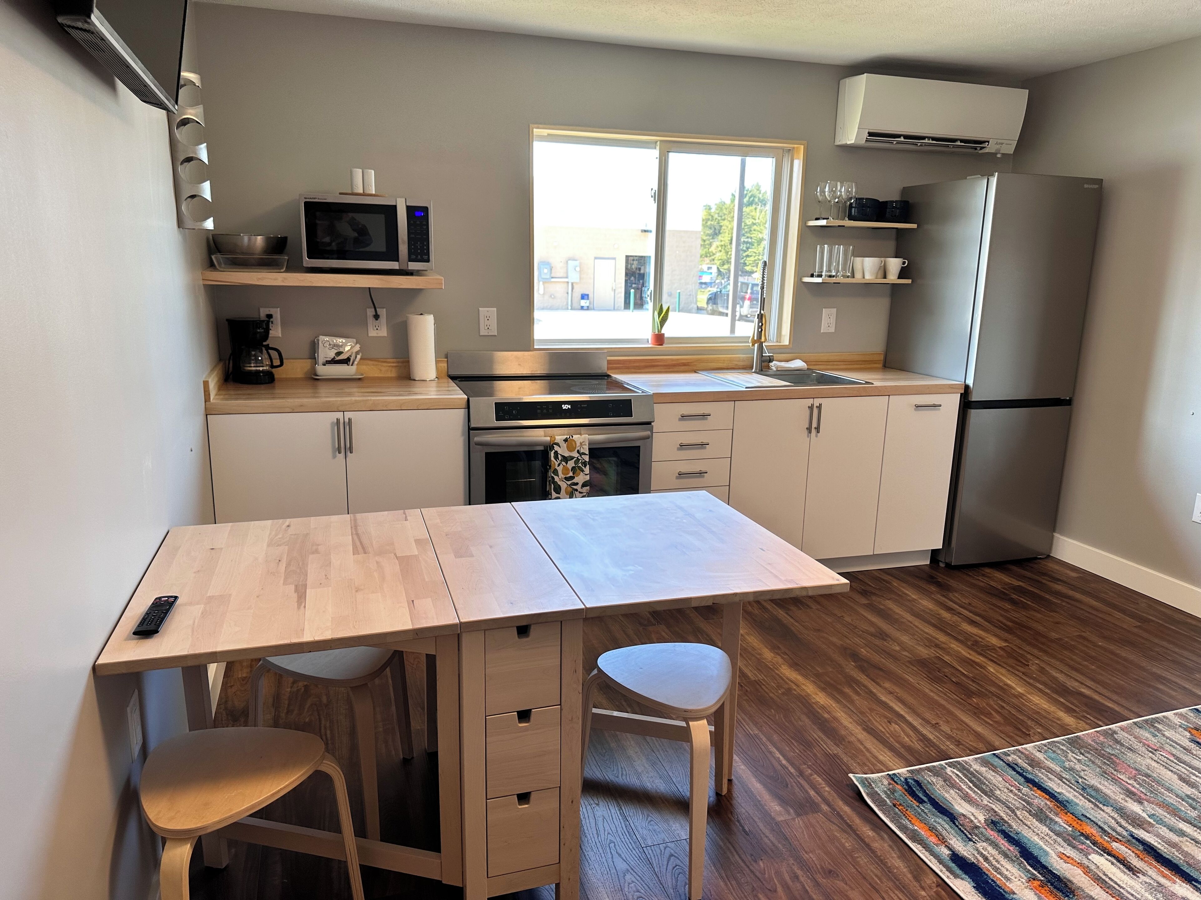 A compact kitchen with a microwave, oven, and refrigerator. There is a small dining table with two chairs and a rug on the floor.