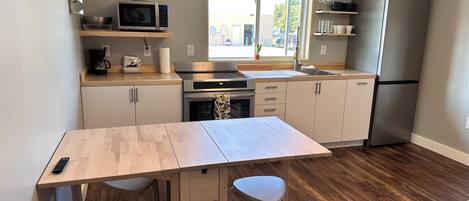 A compact kitchen with a microwave, oven, and refrigerator. There is a small dining table with two chairs and a rug on the floor.